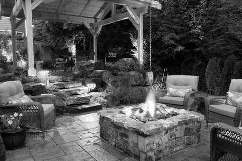 Custom covered patio with a stone fire pit and lounge seating by Alderwood Landscaping
